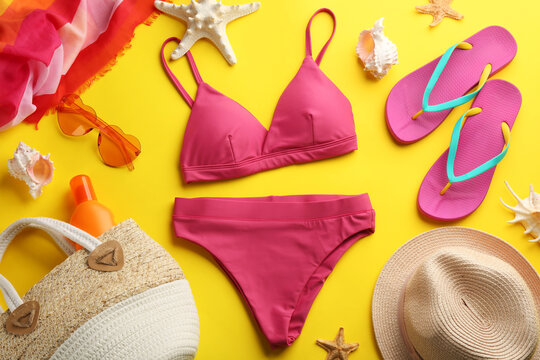 Beautiful pink bikini and beach accessories on yellow background, flat lay