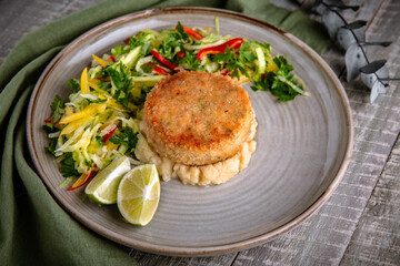 Crab cutlet on a pillow of celery puree with a salad of fresh vegetables and herbs. Delicious, healthy, nutritious dietary meal. Still life in gray-green shades.