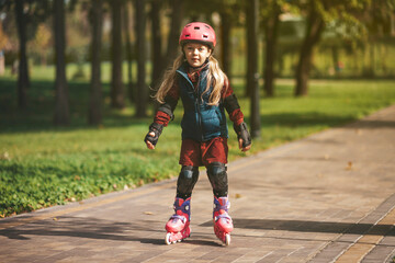 Fototapeta premium Cute preschooler girl is rollerblading in the park.