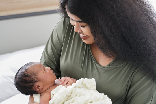 Portrait of African mom carrying adorable newborn baby in her arm. Happy lovely African American family mother and son at bedroom