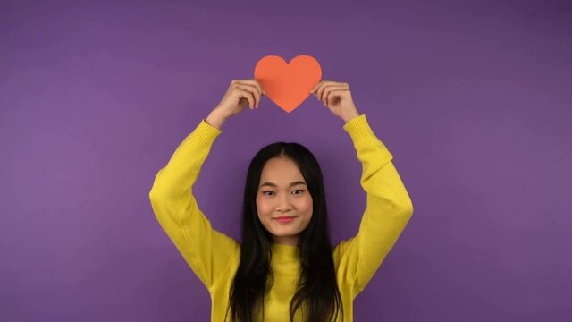 Free space. portrait of a woman with a red heart heart. Isolated young Asian woman on purple background. 4K
