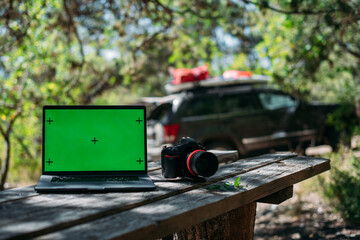 Open laptop and camera on a wooden table at a camping in the mountains