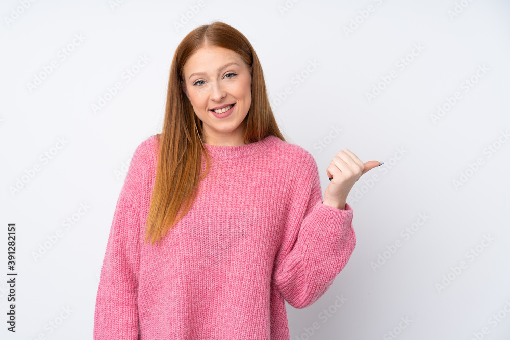 Wall mural young redhead woman with pink sweater over isolated white background pointing to the side to present