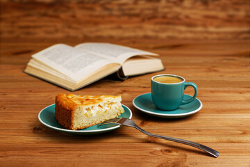Piece of apple pie, cup of coffee espresso and open book on wooden table. Shallow focus.