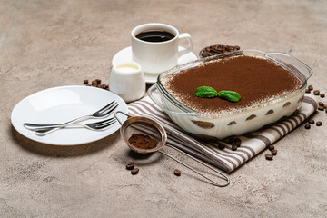 Traditional Italian Tiramisu dessert in glass baking dish and cup of fresh hot espresso coffee on concrete background
