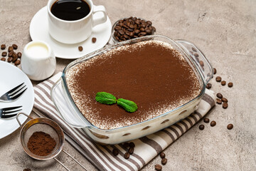 Traditional Italian Tiramisu dessert in glass baking dish and cup of fresh hot espresso coffee on concrete background