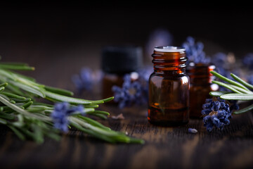 Rosemary and lavender essential oils in dark glass bottles on wood