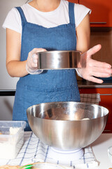 The girl sifts flour through a sieve into a metal bowl that stands on a scale.