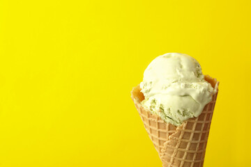 Delicious ice cream in waffle cone on yellow background, closeup. Space for text