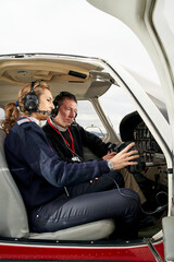 Pilot in training and flight instructor in the cockpit of an airplane. Female pilot with headphones preparing to fly. He is sitting next to the female instructor and looking at the board. © CarlosBarquero