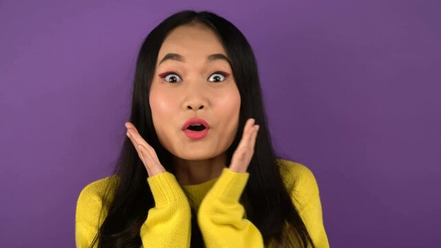 happy young woman with open mouth and big eyes. pretty young asian lady in sweater gesture. isolated purple background. 4K
