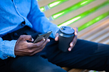 Close up of black man hands holding a cup of coffee and a mobile phone