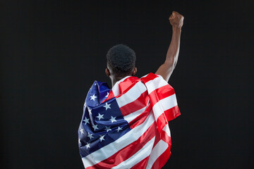 Back view of man wearing american flag standing with raised hand isolated over black background. Concept of patriotism, love for the Motherland, national symbol