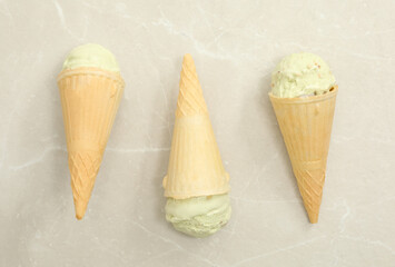 Delicious pistachio ice cream in wafer cones on light grey table, flat lay