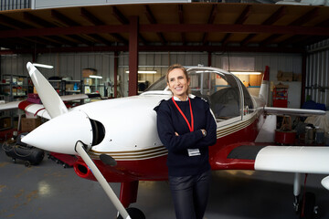 Young female pilot posing smiling in front of her plane inside the hangar. © CarlosBarquero