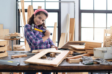 Portrait of a happy young girl holding a hammer in carpentry workshop, looking at camera