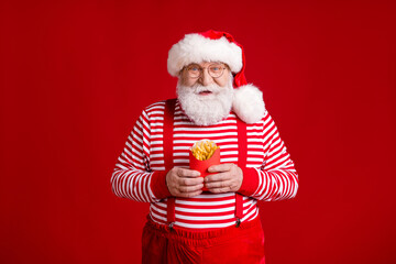 Photo of retired grandpa white beard hold box french fries potato lover attend cafeteria wear santa x-mas costume suspenders spectacles striped shirt cap isolated red color background