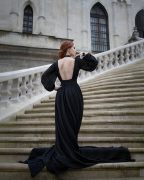 Art photo of a red-haired woman in a black dress on the steps 