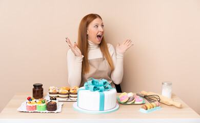 Obraz na płótnie Canvas Young redhead woman with a big cake with surprise facial expression