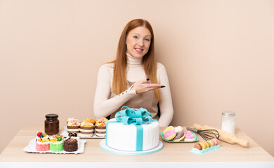Obraz na płótnie Canvas Young redhead woman with a big cake extending hands to the side for inviting to come