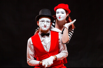Portrait of two mime artists, isolated on black background. Woman appears from behind a man...