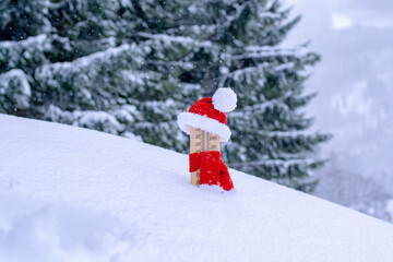 Wooden thermometer dressed up in christmas clothes and placed in fresh snow, trees in background