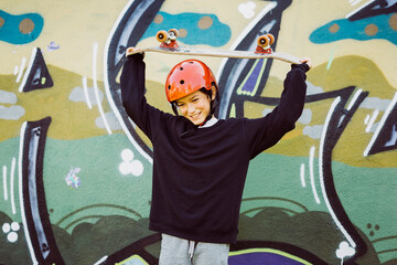 Portrait of a young skater boy wearing  red helmet and playing with an old skateboard, in front of a graffiti mural
