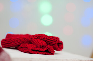 Fototapeta na wymiar New Year card with blurred bright background of bright bokeh. Red knitted gloves are on the bench. Festive winter mood. Warm and cozy clothes for Christmas. Copy space, isolated gift