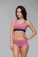 Obraz premium Attractive young brunette woman in pink sportswear is posing isolated on grey background
