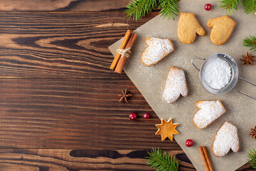 Xmas biscuits on baking paper with powdered sugar and cinnamon sticks on dark wooden table