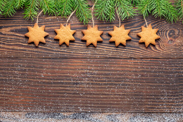 Christmas wood background with homemade star-shaped biscuits hanging from the top among spruce branches