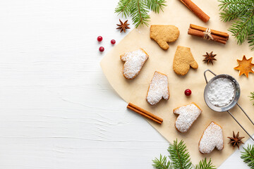 Christmas cookies-mittens on baking paper with powdered sugar and spices on white wooden table