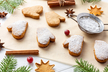 Decoration process of Christmas biscuits on baking paper with powdered sugar on white wooden table
