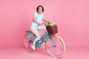 Full length photo of positive smiling woman wear casual riding bike wild flowers isolated pink color background