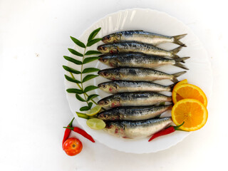 Closeup view of Indian oil Sardine Decorated with herbs and vegetables on a white plate.