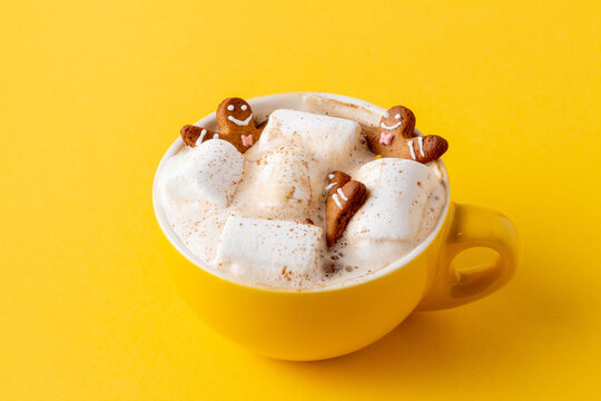 Gingerbread men in yellow cup of latte with marshmallow on yellow background