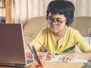 The boy wearing headphones sitting at the table with internet chat skype teacher prepare for exam and using laptop computer for his homework and E-learning for online education. learning kids concept.