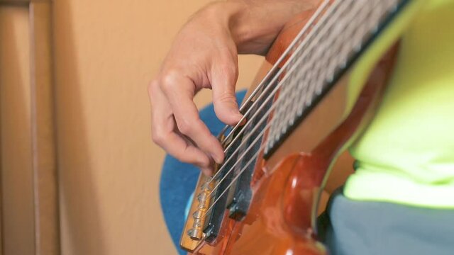 The musician plays a six-string bass guitar in his home Studio. Close up. Soft focus