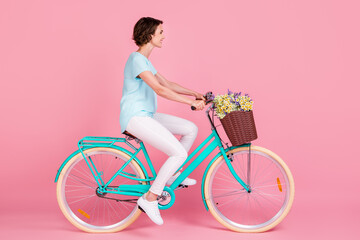 Profile full length photo of cute lovely woman riding vintage bicycle wear blue t-shirt white trousers shoes isolated pink background