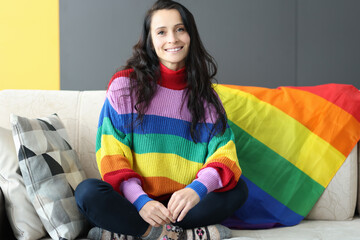 Smiling woman sitting on sofa with lgbt flag. Female homosexuality and recognition concept