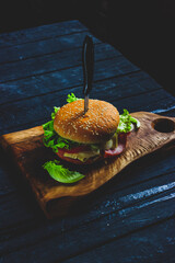 Homemade burger with ham, cheese, salad and pomegranate, pierced by a knife on a wooden board