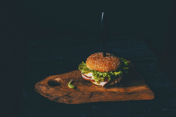 Homemade burger with ham, cheese, salad and pomegranate, pierced by a knife on a wooden board