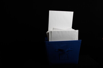 Blue container with large white envelopes inside facing forward on black background.