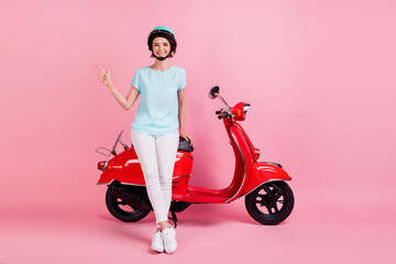 Fototapeta na wymiar Photo of positive pretty young lady stand moped point empty space wear white trousers footwear blue slam t-shirt isolated on pink background