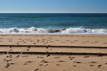 View of Deserted Sandy Beach with Footprints & Breaking Sea Waves against Blue Sky 
