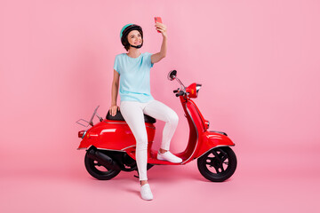 Fototapeta na wymiar Photo of cheerful nice young woman sit moped talk telephone wear pants shoes slam t-shirt isolated on pastel pink background