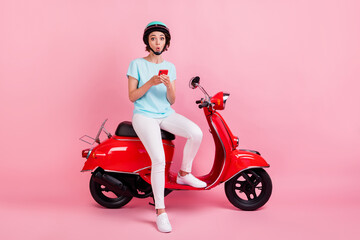 Fototapeta na wymiar Photo of excited pretty young woman sit moped hold telephone dress white trousers sneakers blue slam t-shirt isolated on pink background