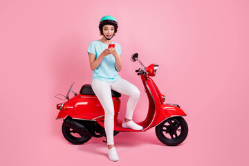 Fototapeta na wymiar Photo of surprised cheerful pretty girl sit moped chat telephone wear white trousers sneakers blue slam t-shirt isolated on pink background