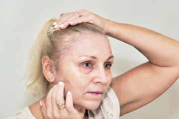 Woman holding her hair applies cream to her face