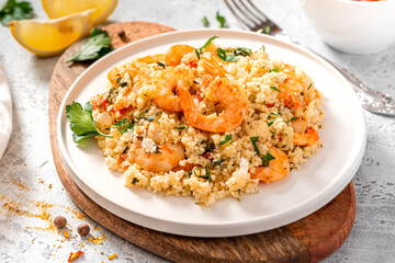 Couscous with shrimps, tomatoes, onions, and herbs in a white bowl close-up. Tasty Moroccan food with couscous and seafood.